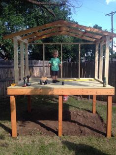 a little boy standing on top of a wooden table in the yard with an umbrella over it