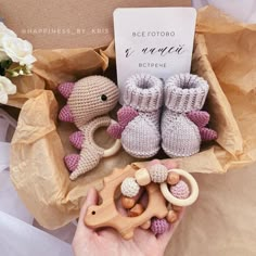 a hand holding a wooden toy with two crocheted baby shoes and a sign