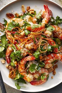 a white plate topped with shrimp and veggies next to a fork on top of a table