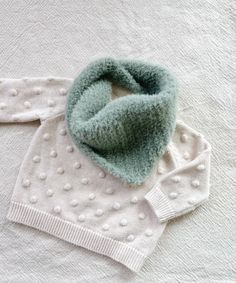 a white sweater and green polka dot scarf laying on top of a bed next to a blanket