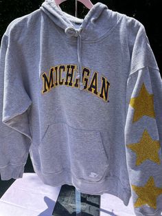 Vintage University of Michigan gray hoodie with gold glitter stars on left sleeve. Lettering is an applique from probably the 90's. Great condition. Fits Medium to Large unisex. Please ask questions before purchasing.  All items are pre -washed. Fall Cotton Sweatshirt With Star Patch, Cotton Sweatshirt With Star Patch For Streetwear, University Of Michigan Sweatshirt, Michigan Hockey, Gameday Fits, Michigan Hoodie, Amazon Cart, Michigan Sweatshirt, Hockey Hoodie