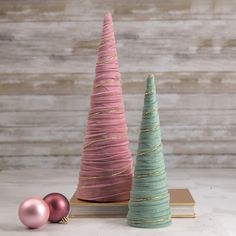 two small christmas trees sitting next to each other on top of a wooden table with pink and green ornaments