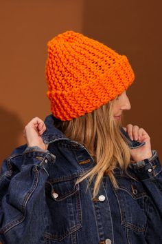 a woman wearing an orange knitted hat and denim jacket with her hands on her hips