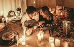 a man and woman sitting on a bed next to each other with candles in front of them