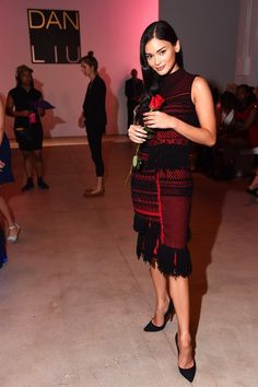 a woman in a black and red dress holding a rose while standing next to other people