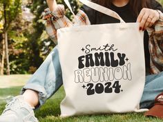 a woman sitting on the grass holding a tote bag that says smith family reunion