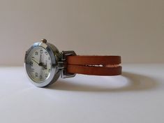 This is a simple women watch with a leather flat cord strap. The style is retro minimalist with a simple distress look. The face of the watch is made in silvered finish alloy, free of nickel and lead, round shape 1 inch diameter. The strap comes in 6 sizes: XS for a 6.00 inches wrist S for a 6.25 inches wrist M for a 6.50 inches wrist L for a 6.75 inches wrist XL for a 7.00 inches wrist XXL for a 7.25 inches wrist If you need another size, please send me a message. The clasp is magnetic and is m Minimalist Everyday Watch With Adjustable Fit, Adjustable Minimalist Watches For Everyday Use, Minimalist Adjustable Watches For Everyday Use, Minimalist Adjustable Everyday Watches, Vintage Leather Bracelet Strap For Watches, Brown Leather Strap Cuff Watch, Leather Wrist Strap For Watches, Everyday Use, Vintage Brown Adjustable Leather Strap Watch Band, Distressed Brown Leather Watch Strap