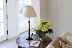 a table with a lamp and flowers on it in front of a door that leads to another room