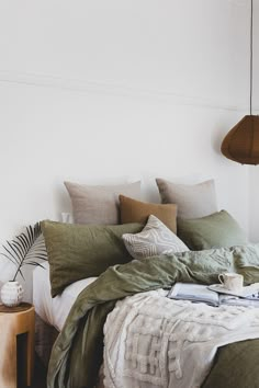 a bed with pillows and blankets on top of it next to a wooden side table