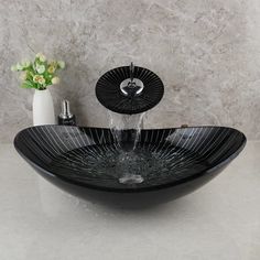 a black bowl sink sitting on top of a counter next to a vase with flowers