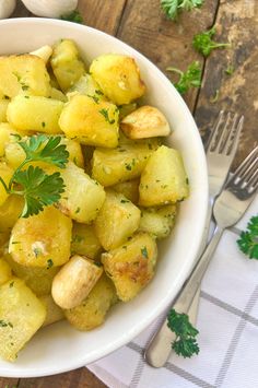 a white bowl filled with potatoes and parsley on top of a table next to silverware