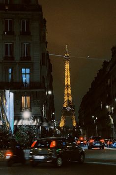 the eiffel tower lit up at night with cars passing by in front of it