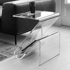 a glass table with a magazine rack on it in front of a couch and chair