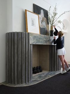 a woman standing in front of a fireplace with a vase on it's mantle