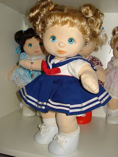 three dolls sitting on top of a shelf next to each other, one is wearing a blue dress and the other has blonde hair