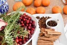 a plate with cinnamon sticks, cranberries and spices on it next to oranges