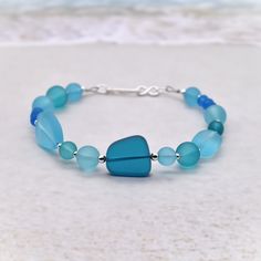 This is a beautiful sea glass bracelet with sterling silver accent beads and a sterling silver infinity clasp. The sea glass beads are recycled glass that have been cultured and gently frosted to resemble glass that has been tumbled in the sea and sand for years.  The colors range from soft aqua to  to a deep Pacific blue.  The shapes are varied and range from 4 mm rondels, 6, and 8 mm round beads to larger nuggets.  The accent beads are sterling silver 2 mm, 2.5 mm, and 3 mm.  The closure is a sterling silver hook that goes into an infinity ring. The bracelet is 7 inches and will fit most.  If you would like a different size, please message me and I will be happy to make one for you! Will arrive in an organza gift bag.  Wonderful and unique gift. All components are .925 sterling silver. Blue Glass Beaded Bracelets For Beach, Adjustable Blue Jewelry Made Of Recycled Glass, Blue Czech Glass Bracelets For Beach, Adjustable Blue Jewelry With Recycled Glass, Blue Czech Glass Bracelet For Beach, Adjustable Ocean-colored Beaded Bracelets For Gifts, Adjustable Blue Recycled Glass Jewelry, Blue Czech Glass Beach Jewelry, Blue Czech Glass Beach Bracelet