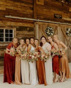 a group of women standing next to each other in front of a wooden building holding bouquets