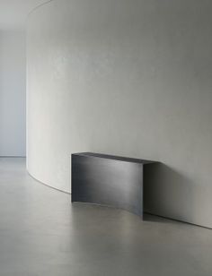 an empty room with white walls and concrete flooring that has a curved shelf on the wall