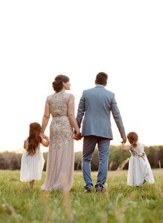 a man and woman holding hands while walking with their two children in a field at sunset