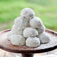 a pile of powdered sugar donuts sitting on top of a wooden table with grass in the background