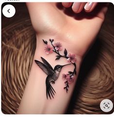 a small hummingbird with pink flowers on it's left arm and wrist tattoo