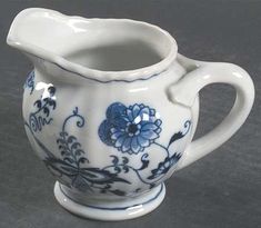 a blue and white porcelain pitcher sitting on a gray tablecloth with flowers painted on it