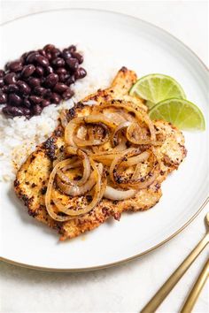 a white plate topped with chicken, rice and beans next to a lime wedged slice