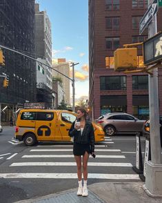 a woman standing on the side of a street next to a yellow taxi and traffic lights