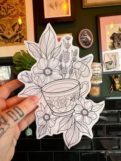 a person holding up a sticker with flowers in a pot on it's side