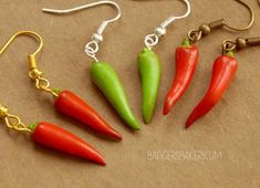 four red and green chili peppers are hanging from gold earwires on brown paper