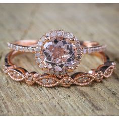 two rose gold wedding rings with an oval cut diamond surrounded by smaller round diamonds, on top of a wooden surface