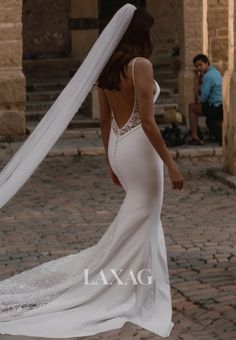 a woman in a white wedding dress is walking down the street with her veil over her head