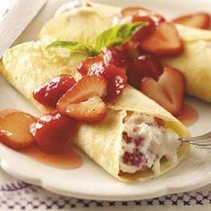 two crepes with strawberries and sauce on a plate next to a fork