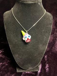 a necklace with a clown face on it and a yellow hat hanging from the neck