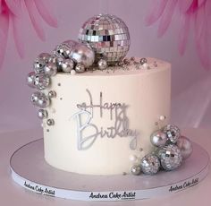 a birthday cake decorated with disco balls and the words happy birthday written on top is white frosting