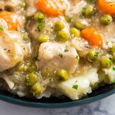 a bowl filled with chicken and vegetables on top of mashed potatoes, peas and carrots