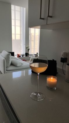 a glass of wine sitting on top of a kitchen counter next to a lit candle