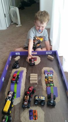 a young boy playing with toy cars in a play table made out of sand and dirt