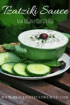 a plate topped with cucumbers and sauce on top of a wooden table next to green leaves