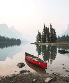 a red canoe sitting on the shore of a lake