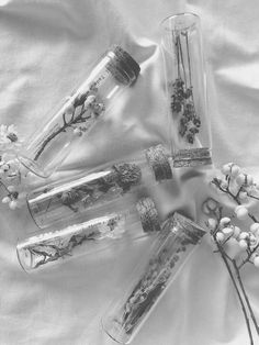 four glass bottles with flowers in them sitting on a white cloth covered surface, one is empty and the other has dried berries