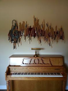 an old piano is sitting in front of a wall with sticks hanging on it's side