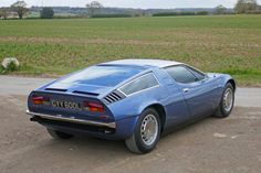 a blue sports car parked on the side of the road in front of a field