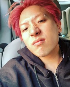 a man with pink hair and piercings sitting in the back seat of a car