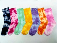 six pairs of tie - dyed socks are lined up on a white surface, all in different colors