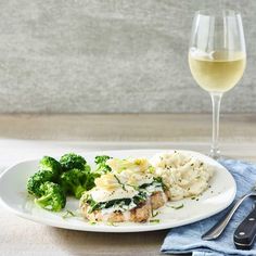 a white plate topped with meat and veggies next to a glass of wine