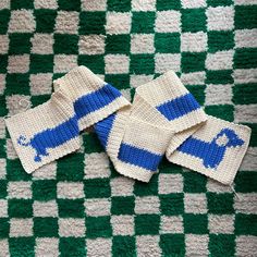 two knitted mitts laying on top of a green and white checkered blanket