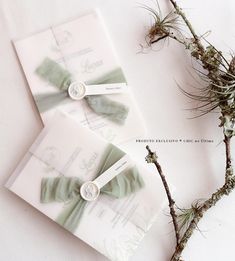 two pieces of paper with bows on them sitting next to some branches and twig