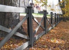 a fence that is next to a tree with leaves on the ground in front of it